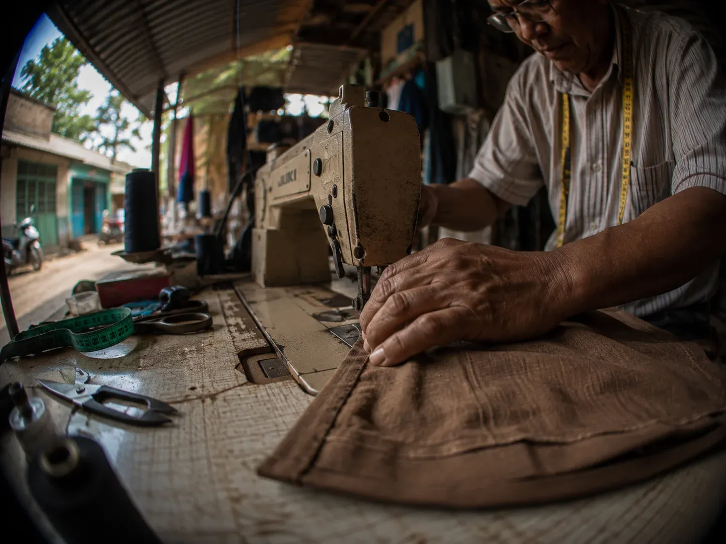 Hombre mayor trabajando concentrado en una máquina de coser dentro de un taller textil, representando la manufactura colombiana.