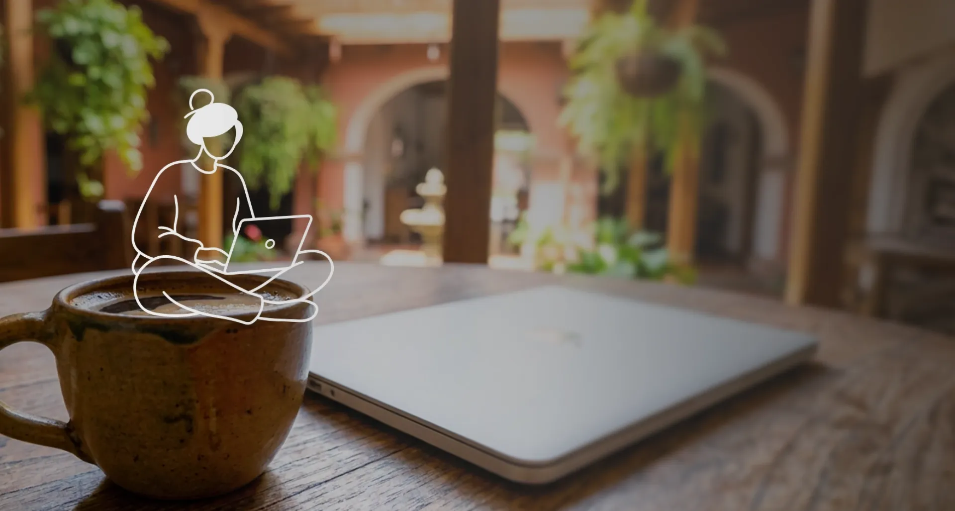 Taza de café rústica y laptop sobre una mesa de madera en un patio colonial colombiano.